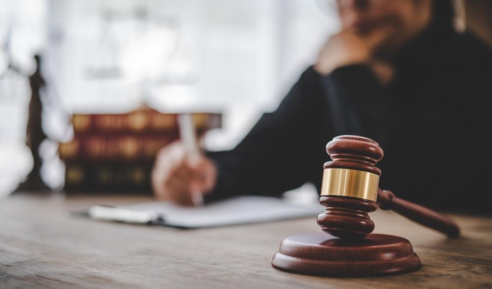 Gavel on a desk with a person writing on a document in the background