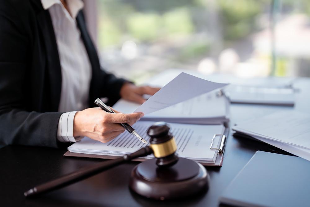 Person in a suit holding a pen and reviewing documents at a desk with a gavel