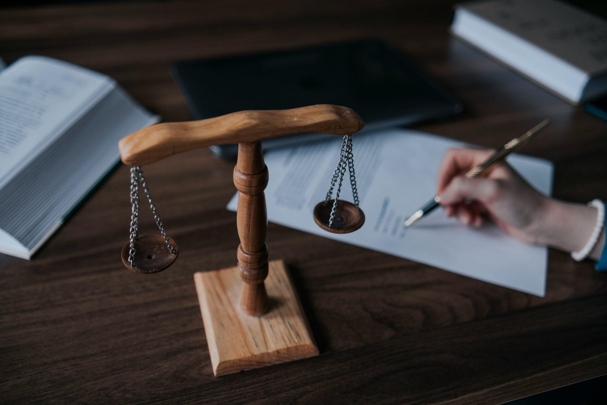 Lawyer writing on paper with a pen, with scales of justice in the background symbolizing legal balance and fairness.