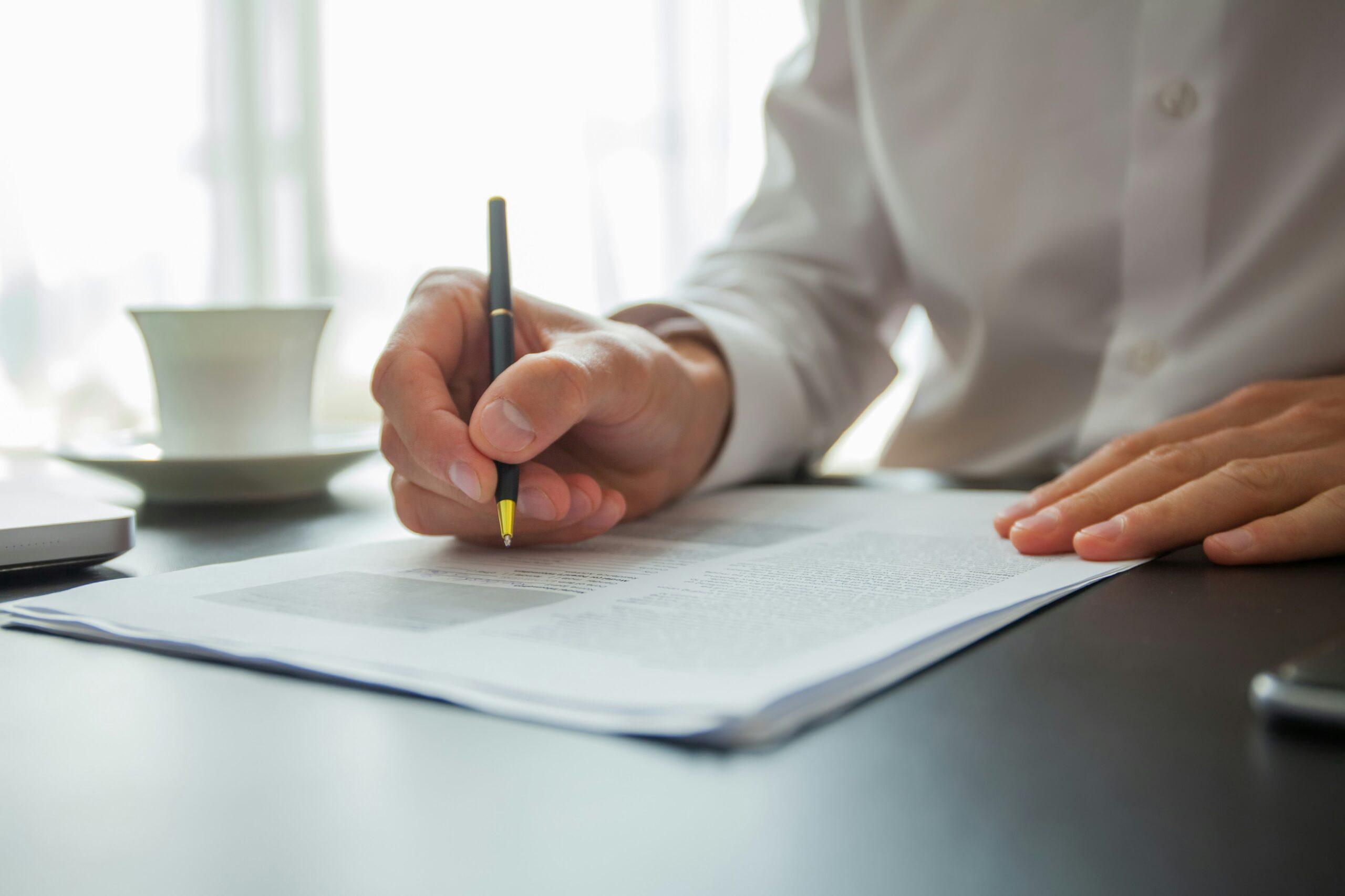 A person writes on a piece of paper with a pen, focused on their task in a well-lit environment.