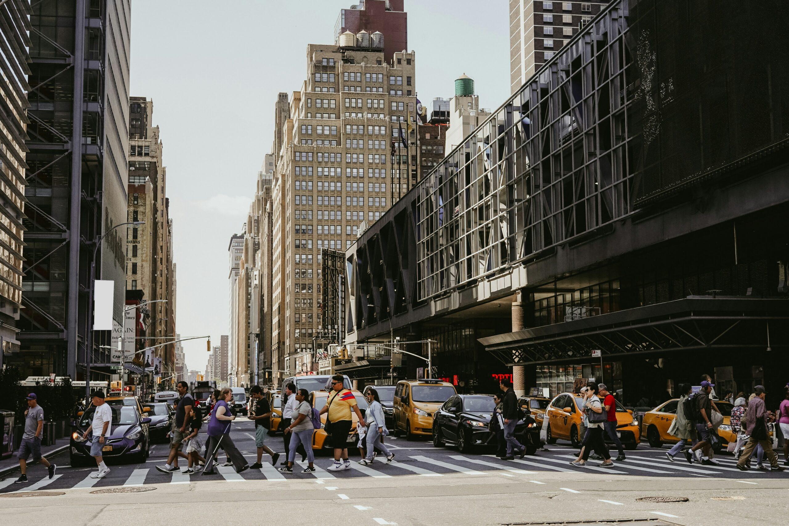 A bustling city street filled with pedestrians crossing at a crosswalk, surrounded by tall buildings and traffic.