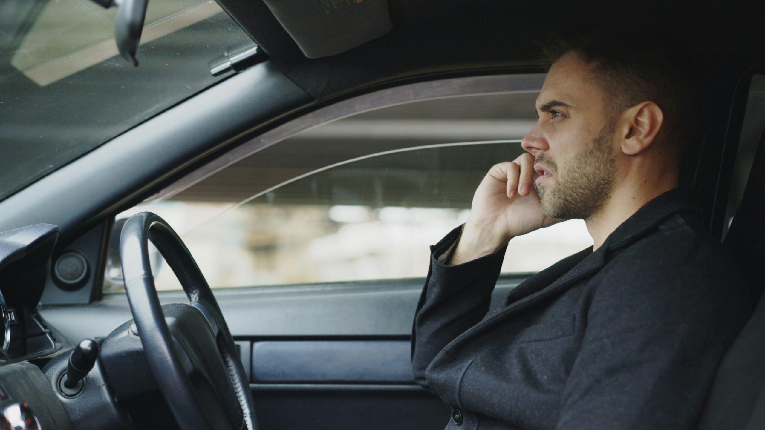 A man sitting in a car, engaged in a conversation on his cell phone.