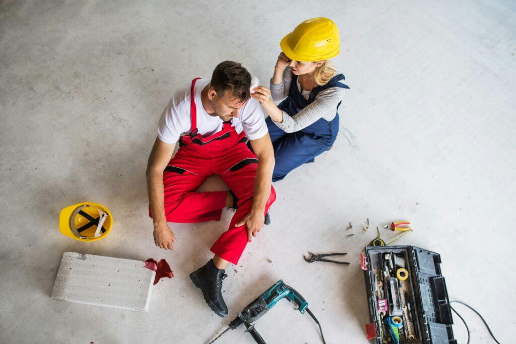 A man and woman in hard hats sit on the floor surrounded by tools, engaged in a construction project.