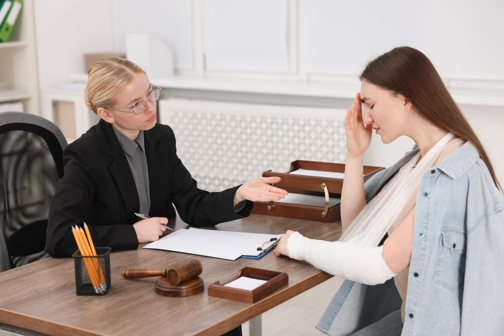A woman with a broken arm sits at a desk with a lawyer, discussing legal matters in a professional setting.