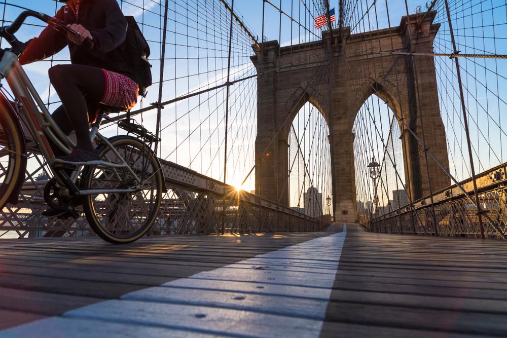 Person riding a bicycle across the Brooklyn Bridge at sunrise