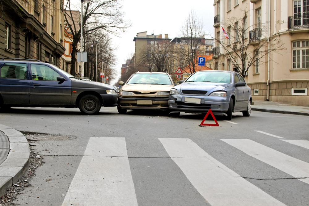 Car accident at an intersection involving three vehicles with a warning triangle placed on the roadway near a crosswalk.