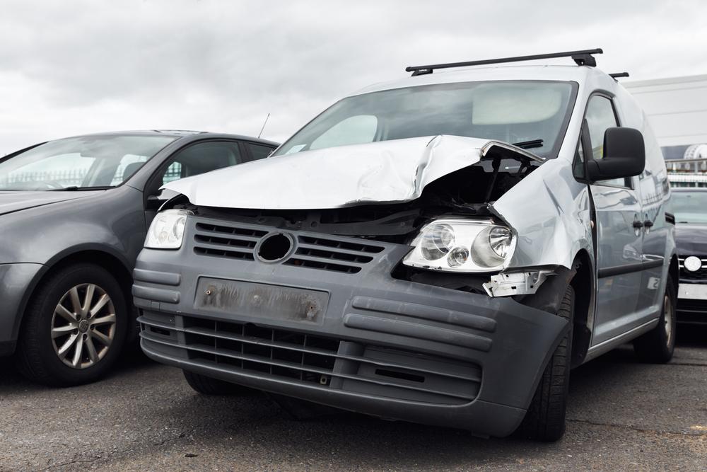 Van with a crushed hood and front-end damage parked among other cars