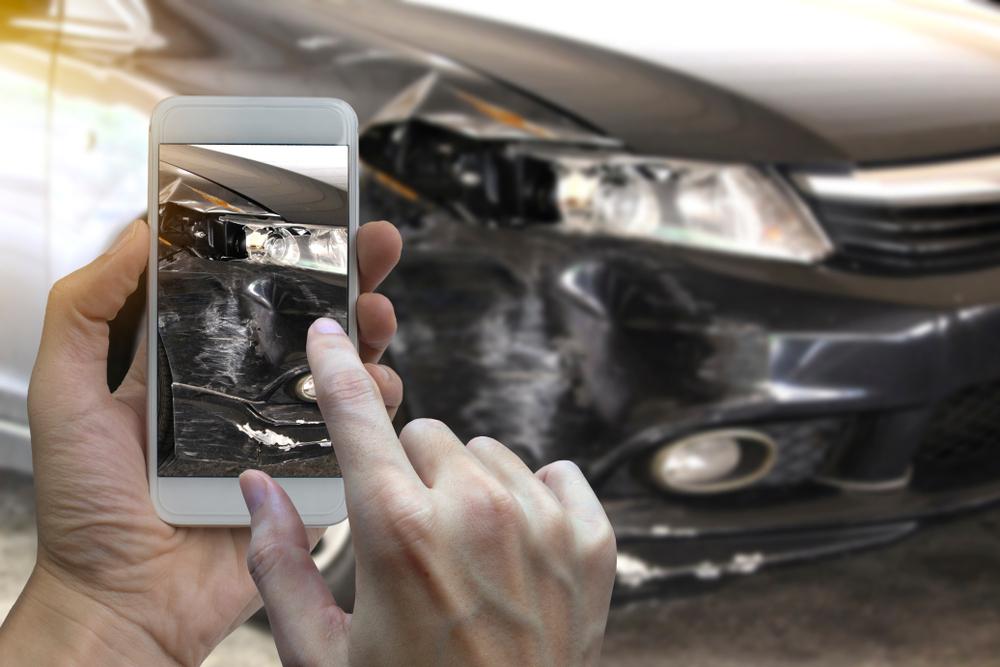 Person photographing damage to the front of a car with a phone