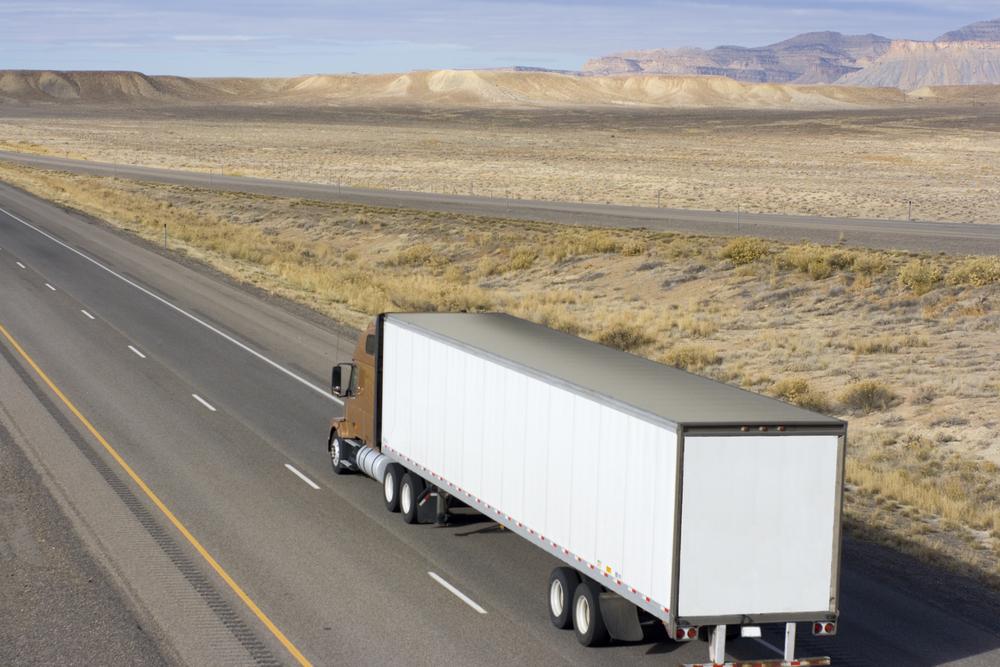 Semi-truck traveling on a highway through a desert landscape