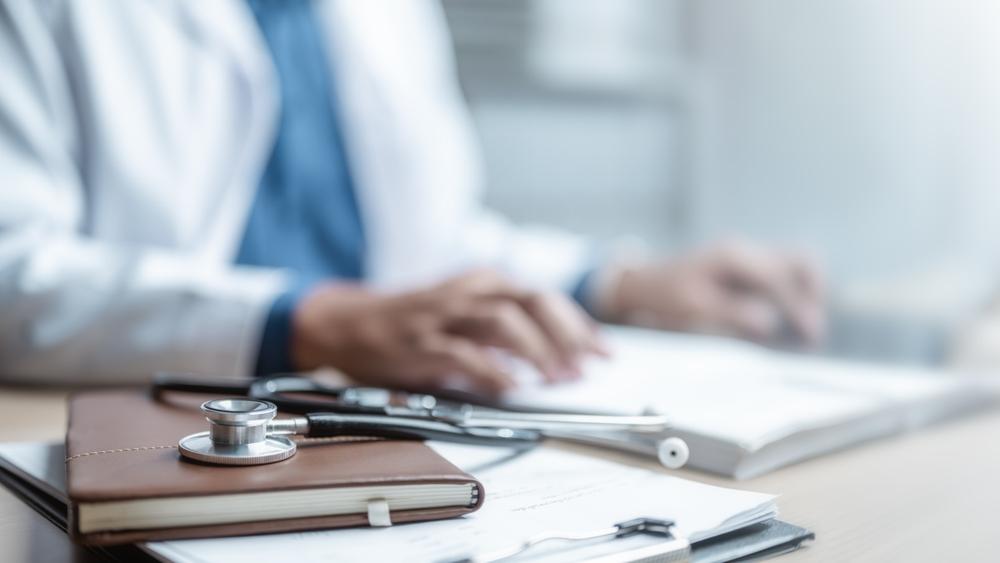 Stethoscope on a notebook in the foreground with a doctor reviewing paperwork behind