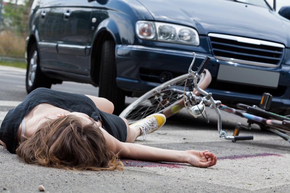 Injured cyclist lying on the pavement beside a fallen bicycle in front of a dark van