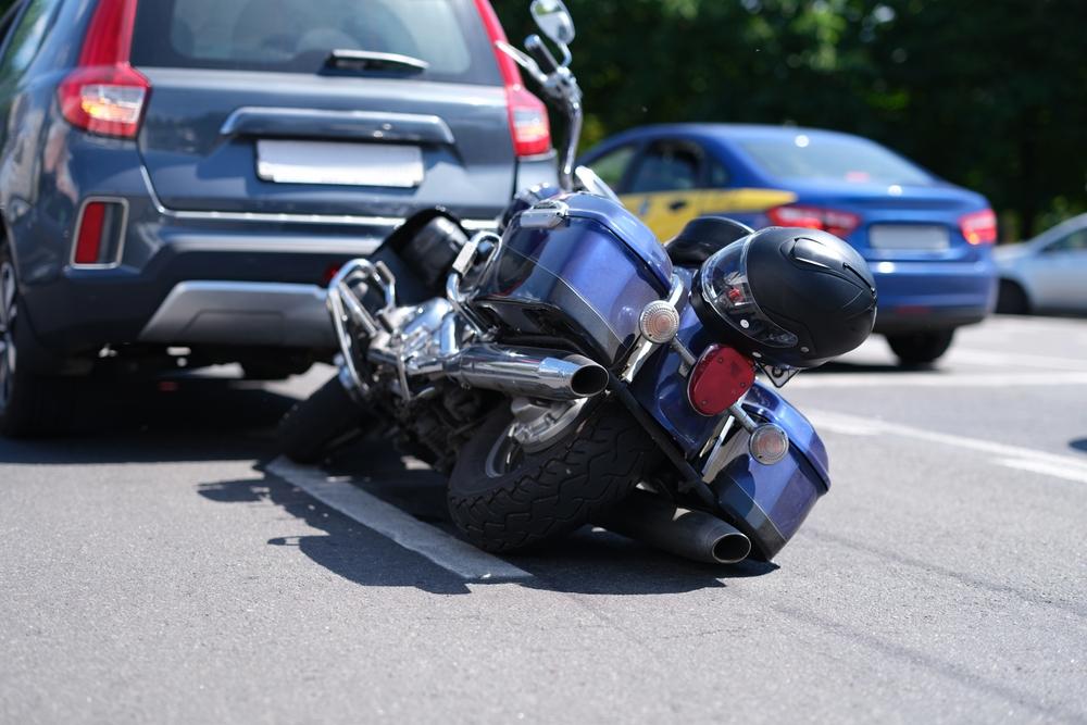 Blue motorcycle with helmet down on the road after a collision with a gray SUV in city traffic