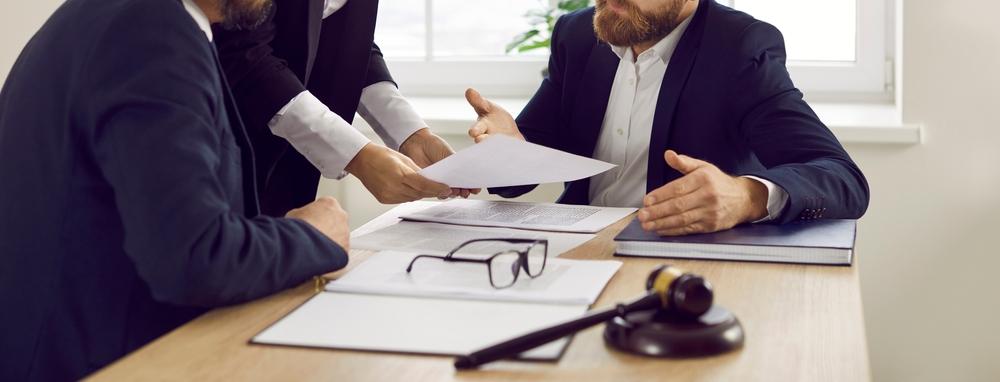 Three people in suits reviewing legal documents at a desk with a gavel